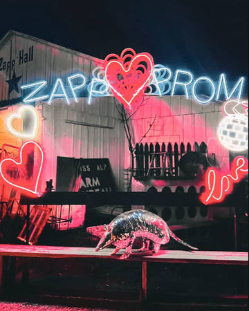Neon sign with 'Zapp & Prom' and a metallic armadillo sculpture on a stage.