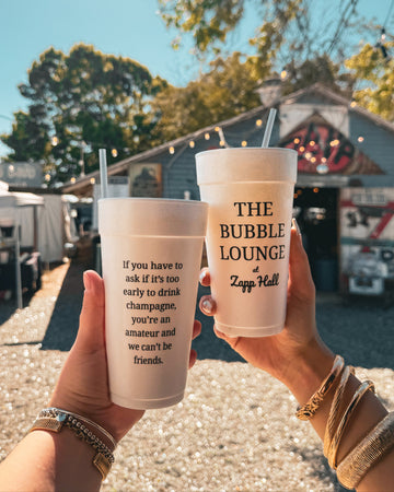 Two hands holding cups with text, one from 'The Bubble Lounge' and a quote, against a casual outdoor background.