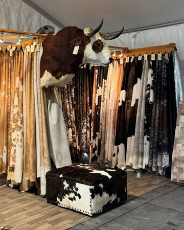 Display of cowhide rugs and a cowhide ottoman in a store setting.