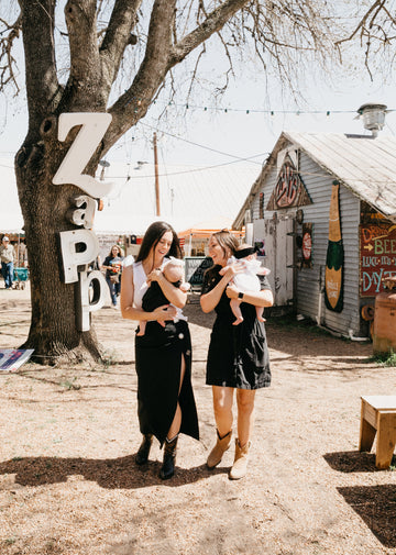 Two best friends holding babies in front of Zapp Hall