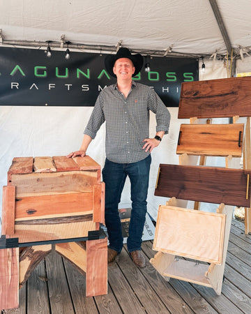 Man standing next to wooden furniture pieces with 'Laguna Beach Craftsman' banner in the background