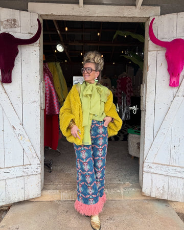 Person in colorful outfit standing in a doorway with pink bull skulls on white doors.