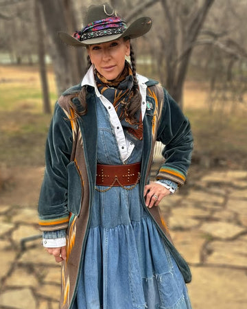 Person in cowboy attire with a long coat and hat, standing outdoors.
