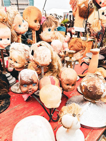 Vintage doll heads and parts on a table at an outdoor market.