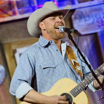 Man in cowboy hat playing guitar and singing into microphone on stage