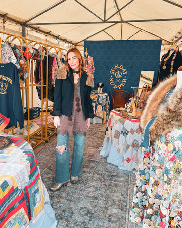 Woman standing inside a tent with various clothing and decorative items on display