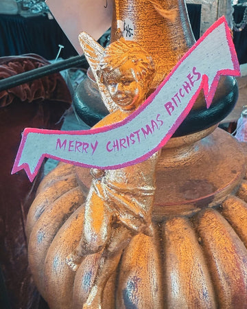 Decorative pumpkin with a cat figurine and 'Merry Christmas Bitches' banner on a smartphone screen.