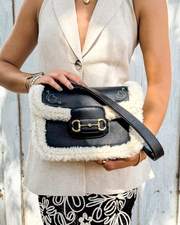 Person holding a black handbag with a fluffy texture against a white background