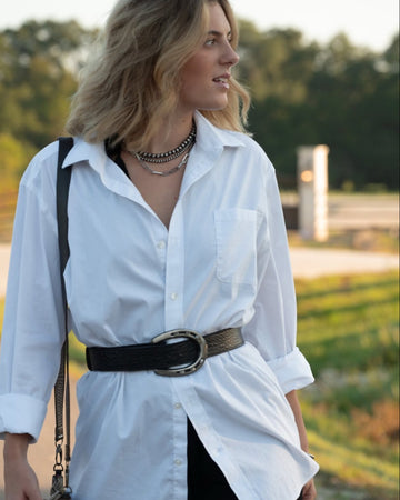 Woman wearing a white shirt with a black horse shoe belt outdoors