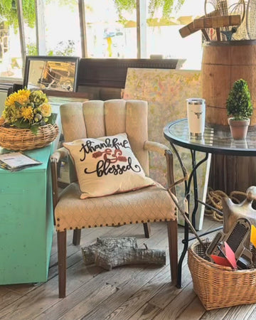 Chair with a 'thankful and blessed' pillow in a cozy indoor setting with decor elements.
