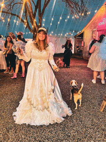 Woman in a white lace dress with a dog at a festive outdoor event.