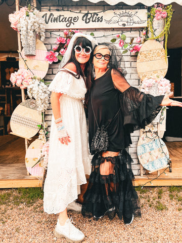 Two women posing in front of a 'Vintage Bliss' backdrop with decorative elements.