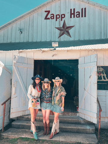 Three women in cowboy hats and boots standing in front of a building with 'Zapp Hall' sign.