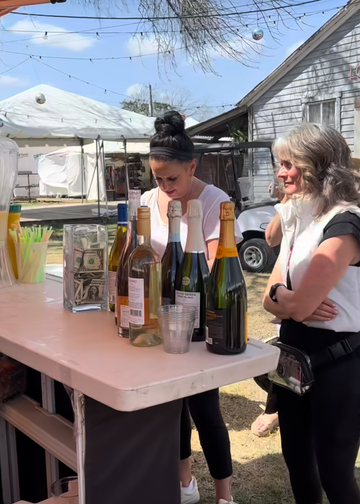 Two women standing around a table with drinks outdoors, with a phone interface overlay.