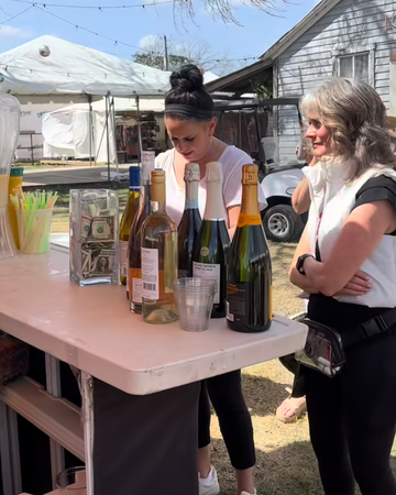 Two women standing around a table with drinks outdoors, with a phone interface overlay.