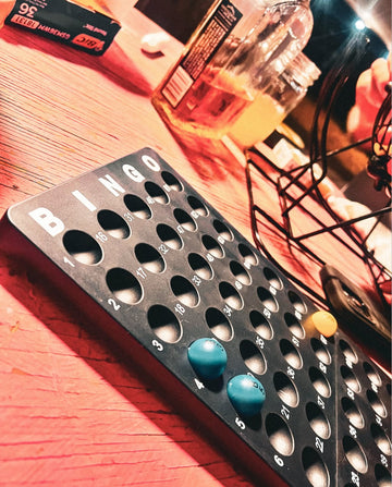 Bingo card with blue markers on a wooden table with a bottle and snacks in the background