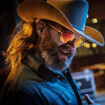 Man wearing a cowboy hat and sunglasses with a blurred background