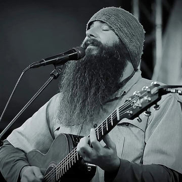 Man with a beard playing guitar and singing into a microphone on stage.