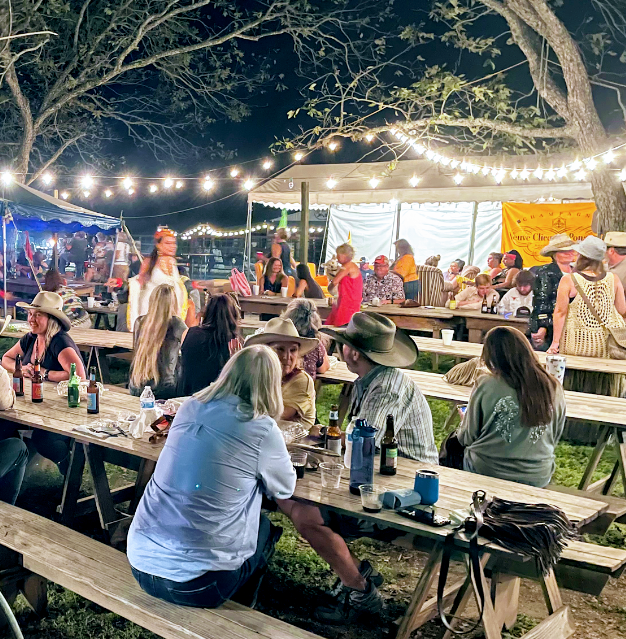 People sitting at outdoor tables under string lights at night.