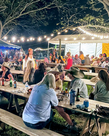 People sitting at outdoor tables under string lights during a gathering.