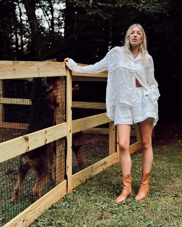 Woman in a white outfit standing next to a wooden fence with a goat inside.