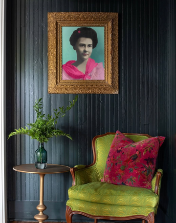 Framed portrait on a dark wall above a green chair with floral cushions.