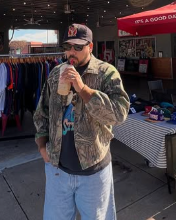 Man drinking from a cup outdoors with a store and red umbrella in the background