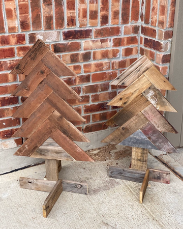 Two wooden Christmas trees made from reclaimed wood against a brick wall.
