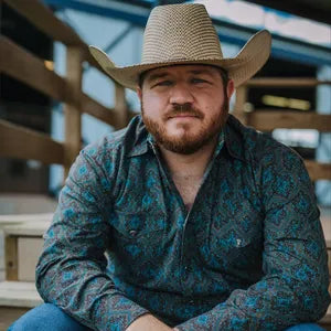 Man wearing a cowboy hat and patterned shirt sitting on wooden steps.